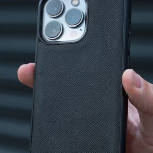 Close-up of a hand holding a black smartphone case against a corrugated background, showcasing design and texture.